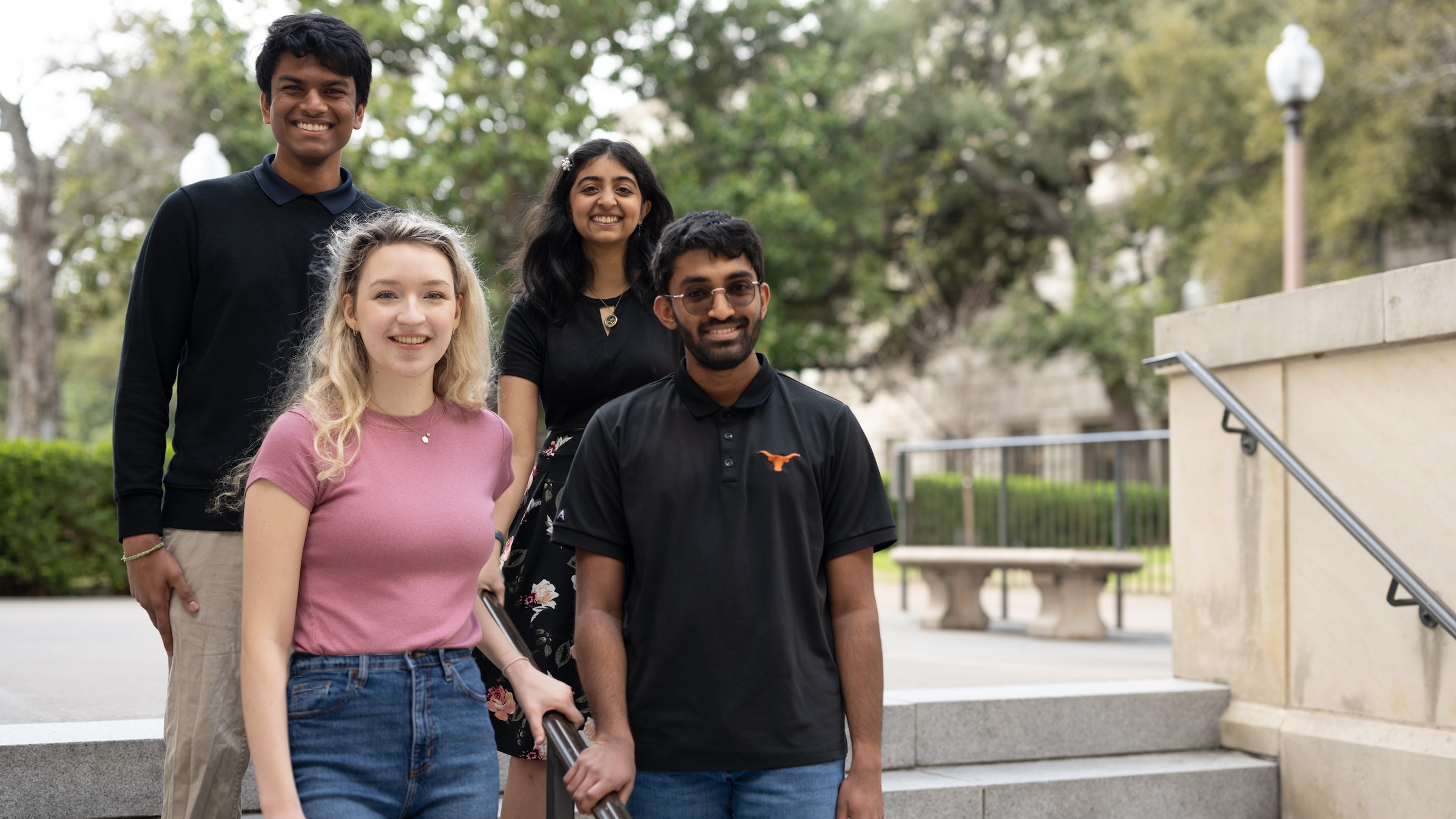 Four students pose on a staircase near a limestone building at UT.
